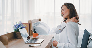 Woman sitting at her desk rubbing her neck in pain.